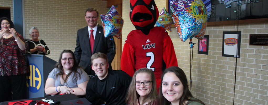 The Peters family poses for a photo sitting behind a table with Red the Cardinal and UIW President Dr. Thomas Evans