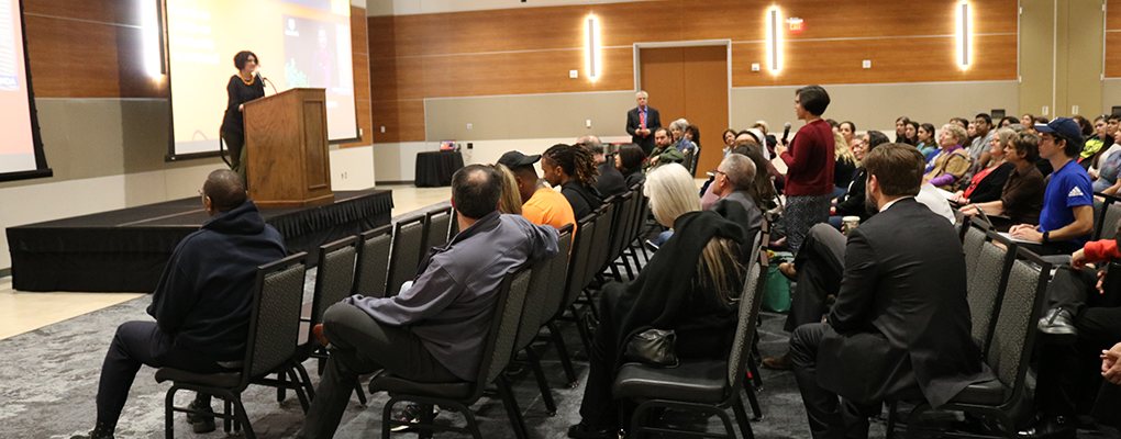 A crowd of people sit and watch a presentation