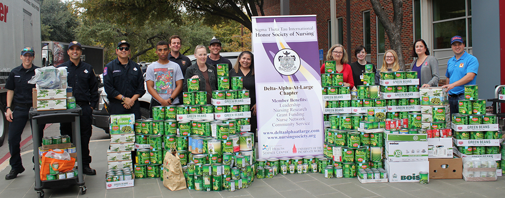 UIW nursing faculty and staff stand with firefighters surrounded by hundreds of cans of green beans