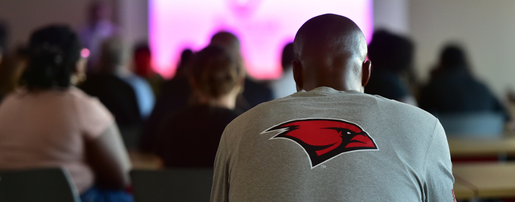 A student wearing a UIW t-shirt looks ahead at a screen
