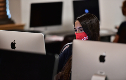 A student wearing a mask works at a computer