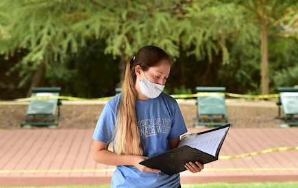A masked student holds a music binder