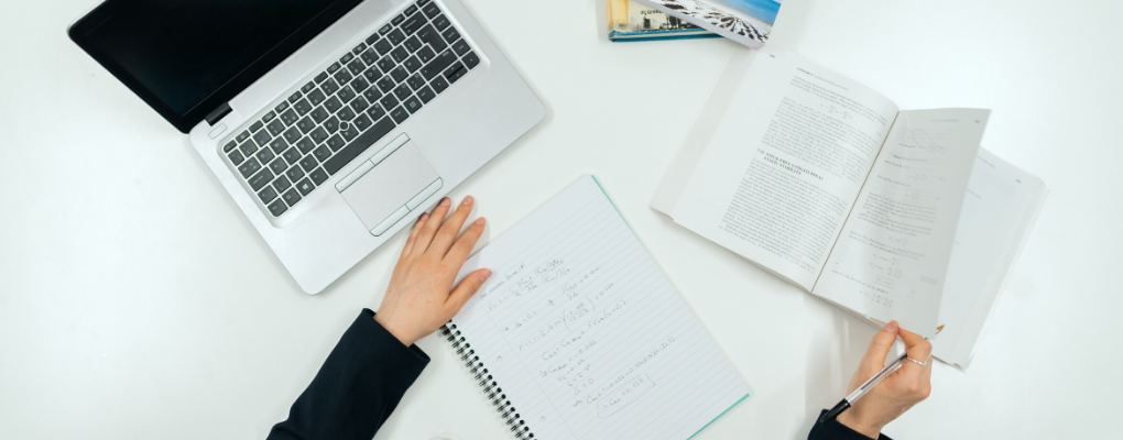 A laptop, paper tablet and books are laid out on a desk