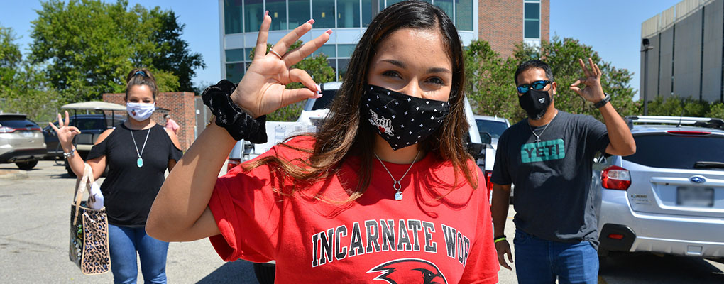 A student and her parents pose for a photo while making the UIW Cardinal hand symbol