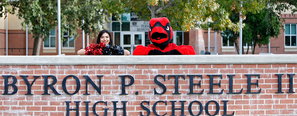 Red the Cardinal and a dance team member peek over a brick wall at Steele High School