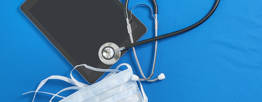 A tablet, surgical mask and stethoscope laid out on a table