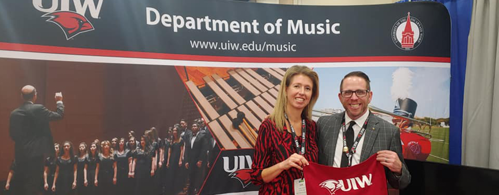 Two people pose for a photo together in front of a UIW music backdrop