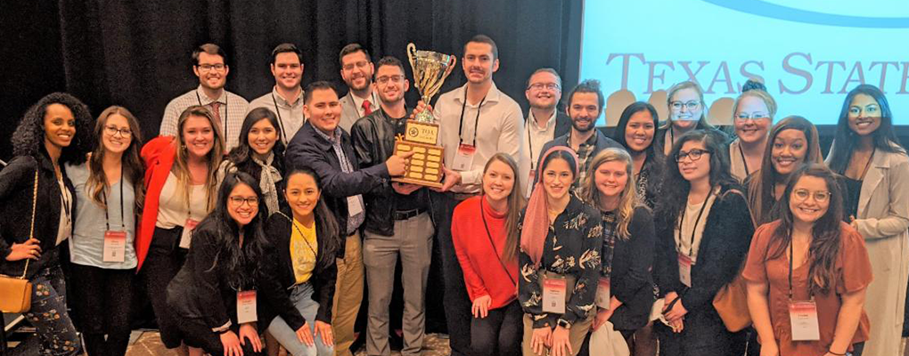 A group of students pose for a photo together holding a trophy