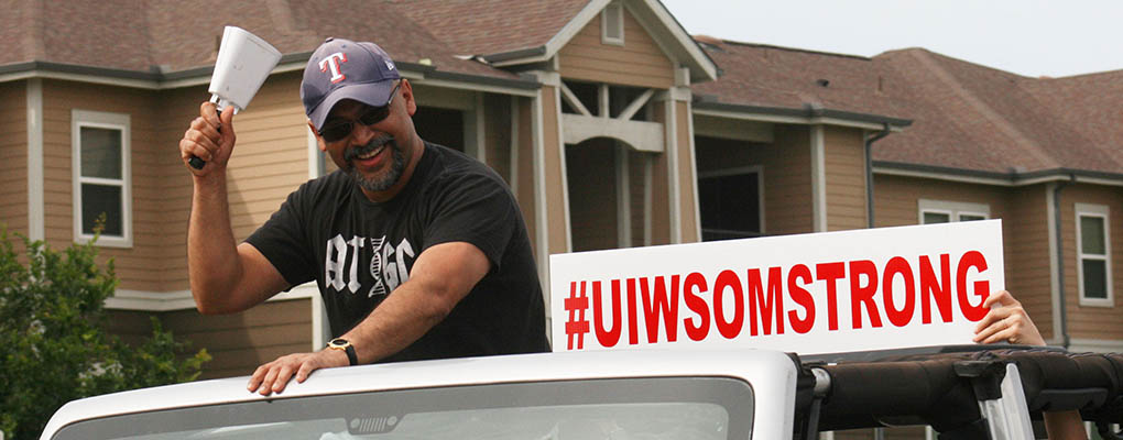 A man stands up in a vehicle holding a sign that says "UIWSOM Strong"