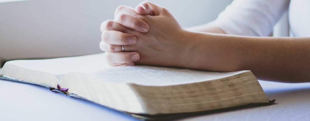 Hands folded in prayer over a Bible