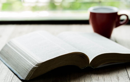 An open Bible next to a coffee mug