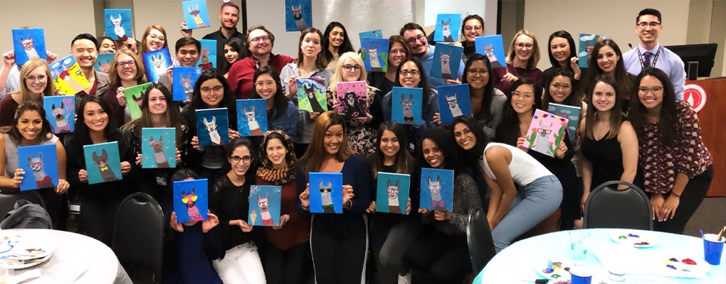 A group of people pose for a photo holding their paintings of llamas 